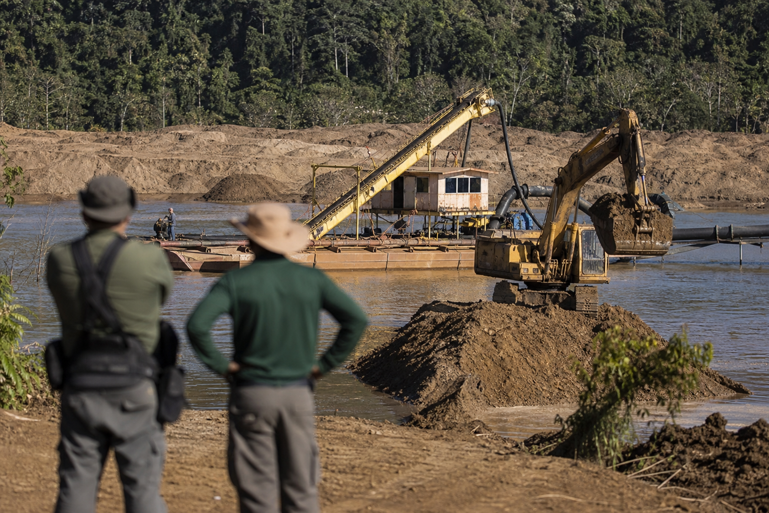 Máquinas pesadas de mineração em área de operação sob fiscalização ambiental, com vegetação nativa ao fundo